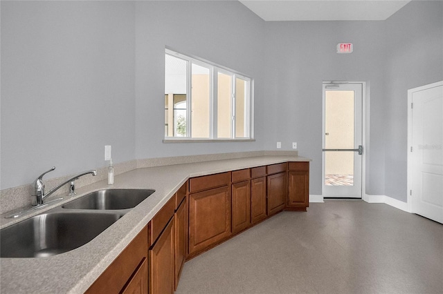 kitchen featuring light countertops, baseboards, a sink, and brown cabinets