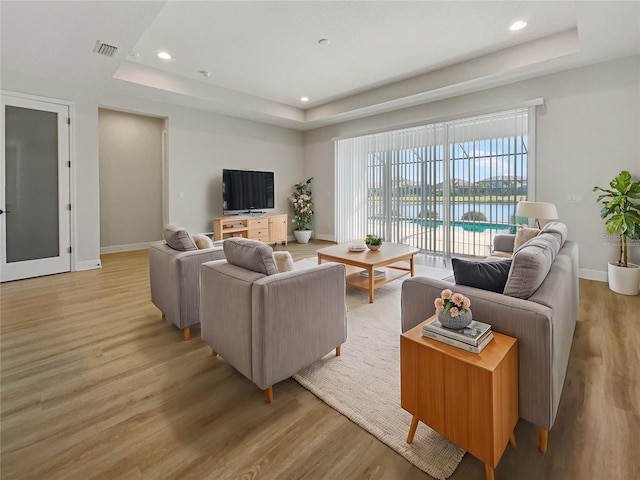 living area featuring a tray ceiling, light wood-type flooring, visible vents, and baseboards