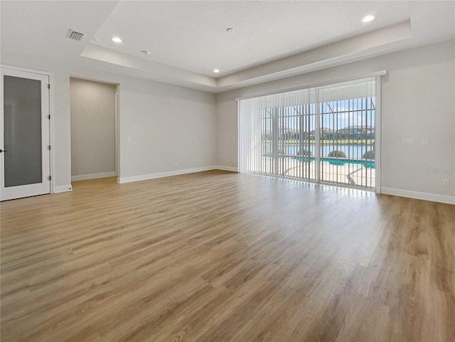 empty room featuring a raised ceiling, visible vents, light wood finished floors, and baseboards