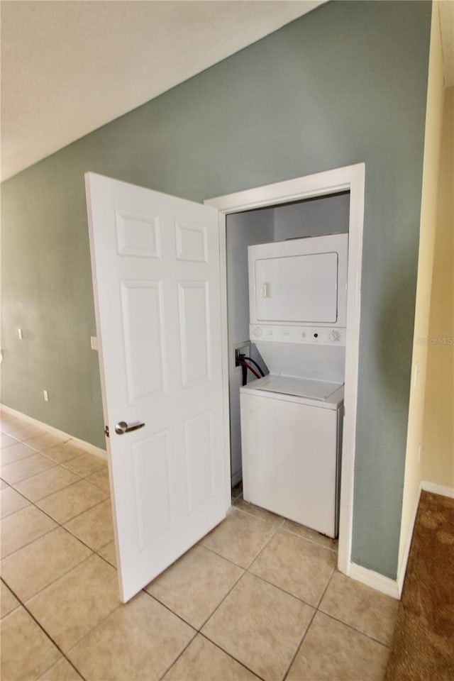 clothes washing area featuring stacked washer and dryer, baseboards, light tile patterned floors, and laundry area