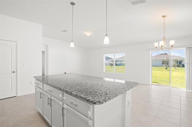 kitchen with light stone counters, light tile patterned flooring, visible vents, a center island, and decorative light fixtures