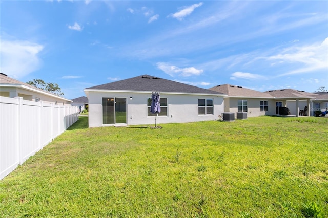 back of property with a yard, stucco siding, fence, and central air condition unit