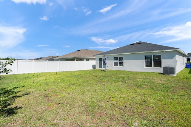 rear view of house with central AC, a shingled roof, fence, a yard, and stucco siding