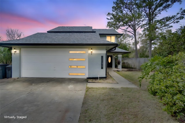 view of front facade featuring a garage, concrete driveway, a shingled roof, and fence