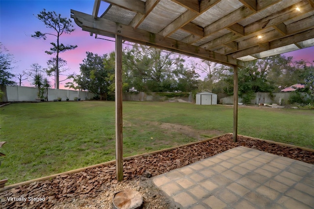 yard at dusk with a patio area, a fenced backyard, an outdoor structure, and a storage shed