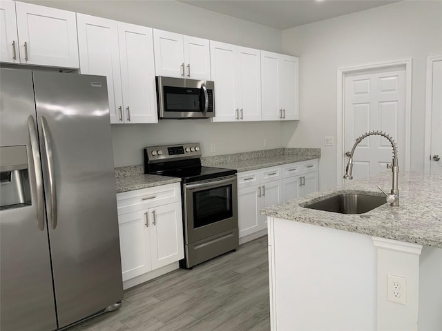 kitchen with light stone counters, light wood-style flooring, stainless steel appliances, a sink, and white cabinetry