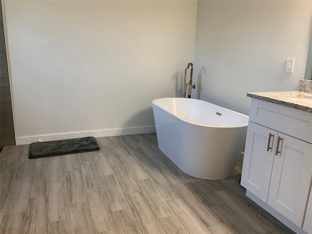 bathroom with a soaking tub, baseboards, wood finished floors, and vanity