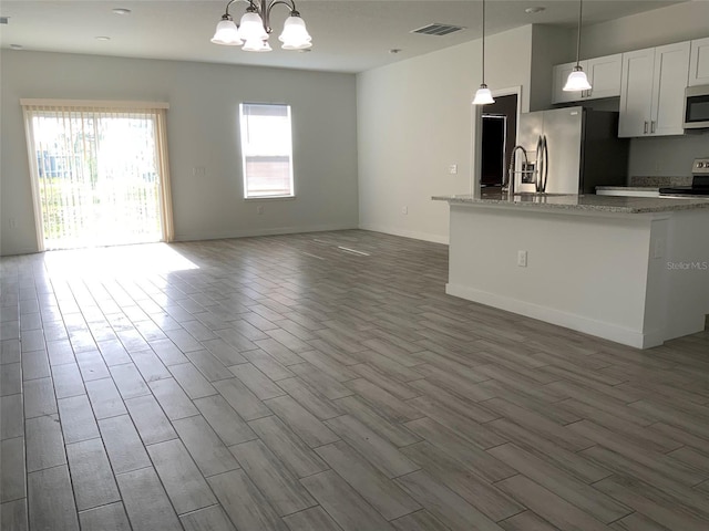 kitchen featuring visible vents, open floor plan, wood finished floors, light stone countertops, and stainless steel appliances