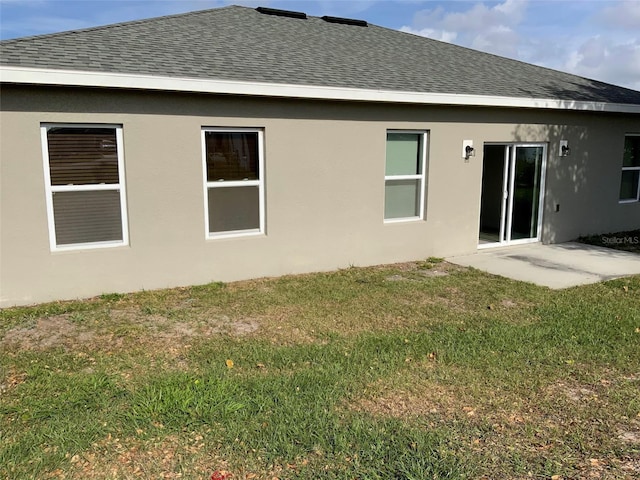 back of property with roof with shingles, a lawn, and stucco siding