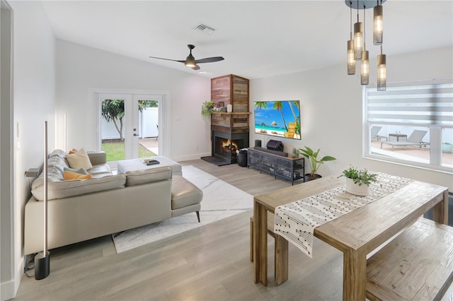 living area with visible vents, french doors, a fireplace, light wood finished floors, and vaulted ceiling