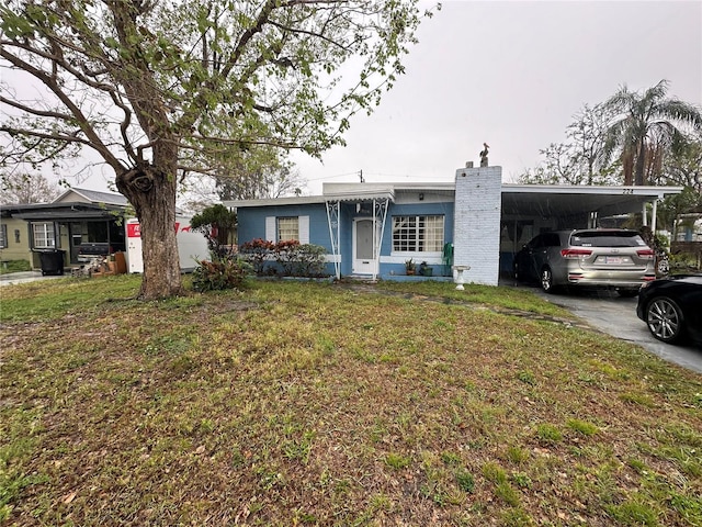 single story home featuring driveway, an attached carport, a chimney, and a front yard