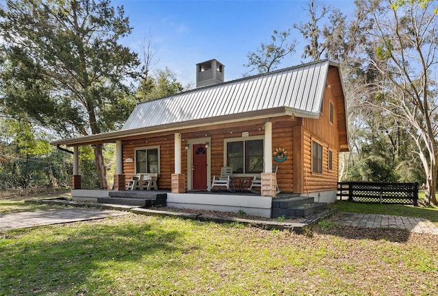 view of front of home with a gambrel roof, a front lawn, covered porch, metal roof, and a chimney