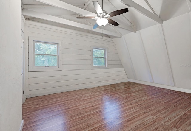 empty room featuring wood walls, lofted ceiling with beams, a ceiling fan, and wood finished floors