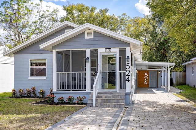 view of front of home with a carport, brick siding, decorative driveway, and a sunroom