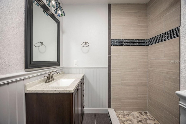 full bath with a wainscoted wall, a tile shower, and vanity