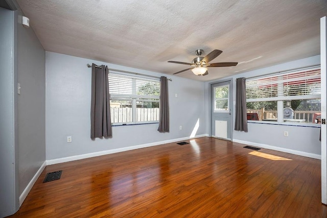 empty room with a wealth of natural light, visible vents, and wood finished floors