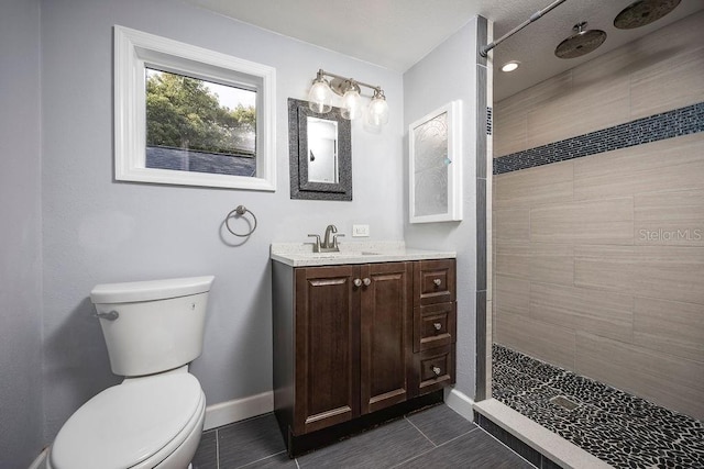 bathroom featuring vanity, a tile shower, toilet, and baseboards