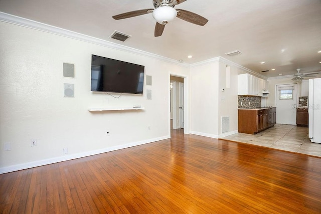 unfurnished living room with light wood finished floors, ceiling fan, visible vents, and crown molding