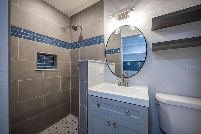 bathroom featuring a textured wall, a tile shower, vanity, and toilet