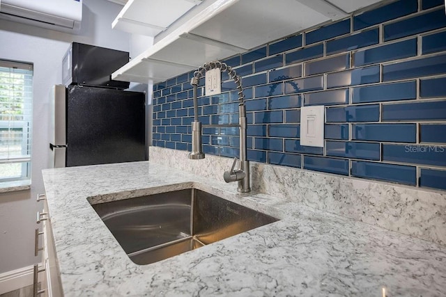 kitchen featuring an AC wall unit, backsplash, freestanding refrigerator, and light stone countertops