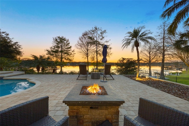 pool at dusk with a patio area, an outdoor pool, an outdoor fire pit, and a water view