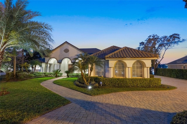 mediterranean / spanish home with a tile roof, a front lawn, and stucco siding