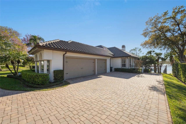 view of front of home featuring fence, a tiled roof, stucco siding, decorative driveway, and an attached garage