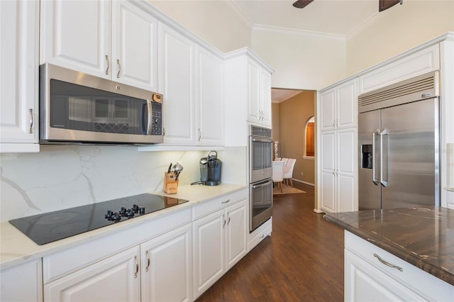 kitchen featuring backsplash, crown molding, arched walkways, white cabinets, and stainless steel appliances