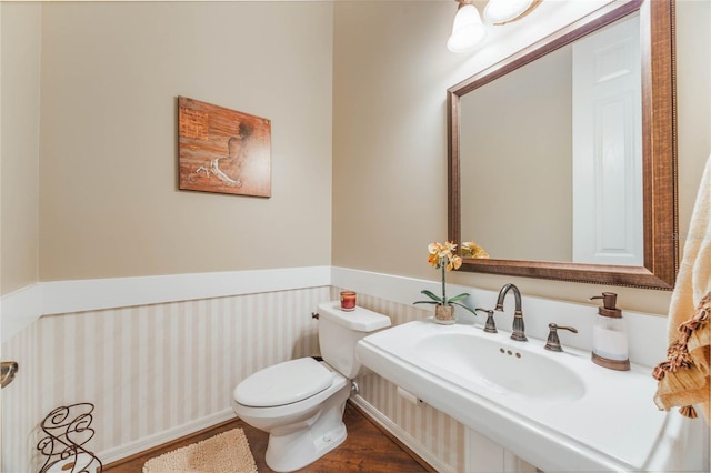 half bath with toilet, wood finished floors, a wainscoted wall, and a sink