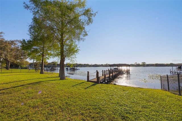 dock area with a yard, a water view, boat lift, and fence