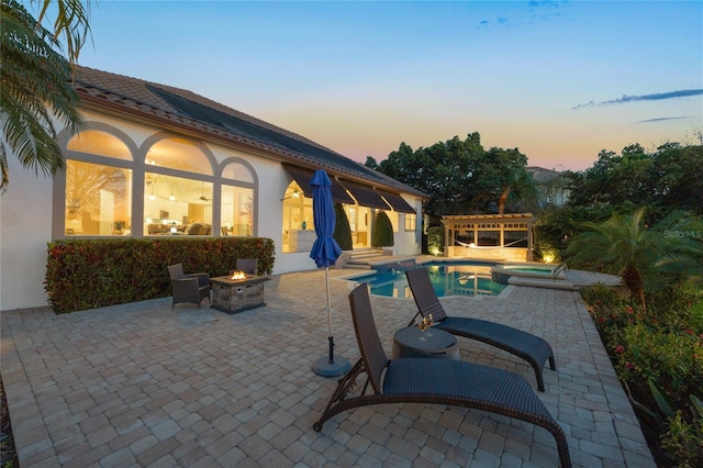 pool at dusk with a patio, a pergola, a pool with connected hot tub, and an outdoor fire pit