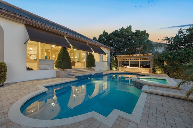 pool at dusk with a patio area and a pool with connected hot tub