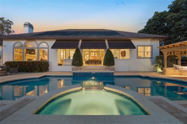 back of property at dusk with a tiled roof, a chimney, and a pool with connected hot tub