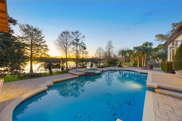 pool at dusk featuring a patio area and a pool with connected hot tub