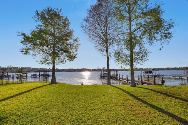 view of dock with a lawn, fence, a water view, and boat lift