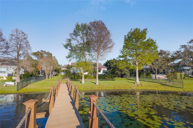 view of dock with a lawn, a water view, and fence