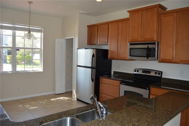 kitchen featuring a sink, appliances with stainless steel finishes, brown cabinets, dark stone counters, and decorative light fixtures