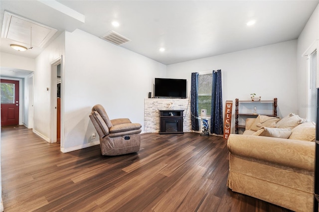 living area featuring dark wood-style flooring, visible vents, attic access, a glass covered fireplace, and baseboards