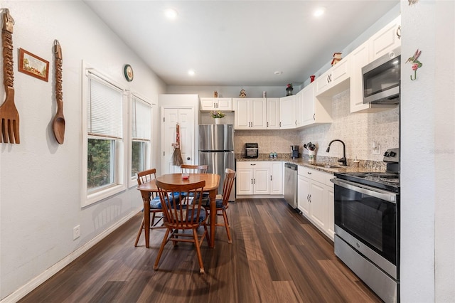 kitchen featuring dark wood-style flooring, a sink, stainless steel appliances, white cabinetry, and backsplash