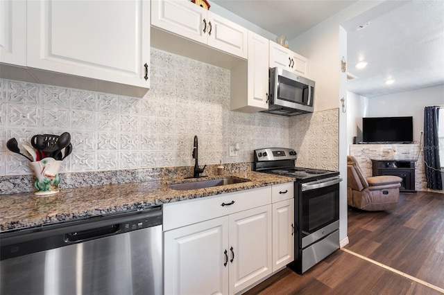 kitchen featuring dark wood finished floors, dark stone counters, appliances with stainless steel finishes, a sink, and backsplash