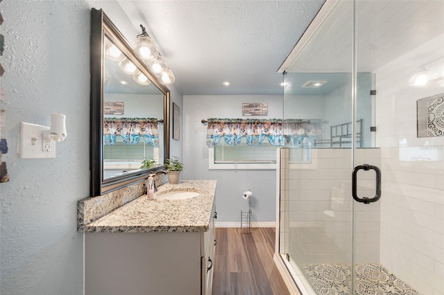 bathroom featuring a textured wall, wood finished floors, a textured ceiling, vanity, and a shower stall