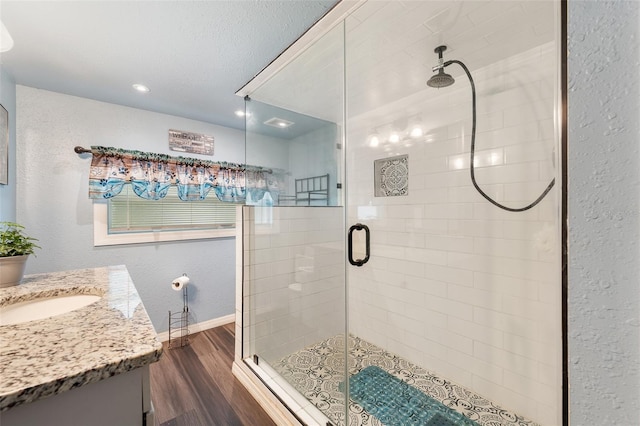 bathroom with a textured wall, vanity, a shower stall, wood finished floors, and baseboards