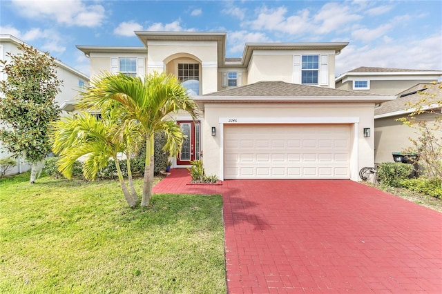 view of front of house with decorative driveway, a front yard, an attached garage, and stucco siding