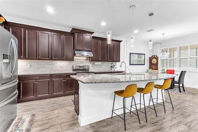 kitchen with a sink, under cabinet range hood, stainless steel appliances, decorative backsplash, and light stone countertops