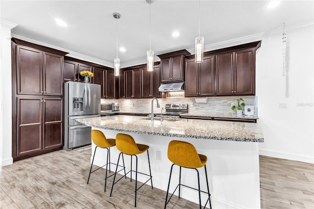 kitchen with under cabinet range hood, stainless steel appliances, a kitchen bar, and a sink