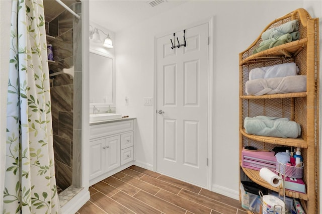 full bath with wood finish floors, visible vents, vanity, baseboards, and tiled shower