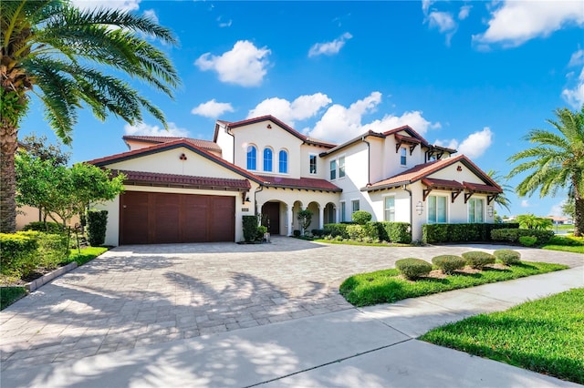 mediterranean / spanish-style house featuring a garage, decorative driveway, a tiled roof, and stucco siding