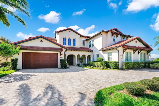 mediterranean / spanish-style house featuring a garage, a tiled roof, decorative driveway, and stucco siding