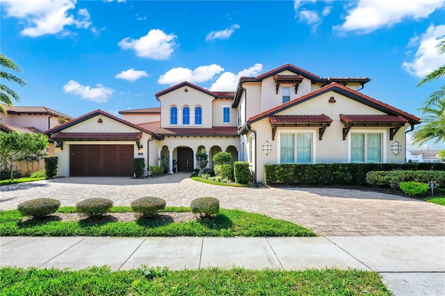 mediterranean / spanish-style house featuring a garage, decorative driveway, a tiled roof, and stucco siding