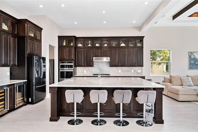 kitchen featuring a breakfast bar area, double oven, fridge with ice dispenser, beverage cooler, and under cabinet range hood